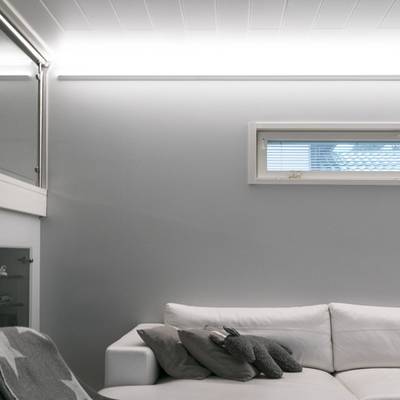 Un salon minimaliste avec de la lumière naturelle, des rideaux de fenêtre et un éclairage LED doux sur des murs gris.
