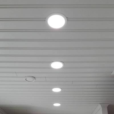 Quatre plafonniers encastrés à LED éclairent une pièce lambrissée blanche. Les panneaux LED ronds éclairent avec un large faisceau.