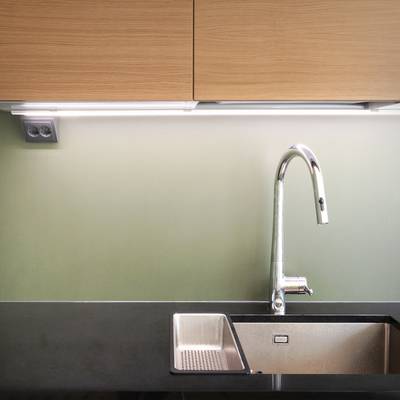 Évier de cuisine éclairé par LED, robinet chromé, comptoir noir et rétroéclairage vert clair sous l'armoire.