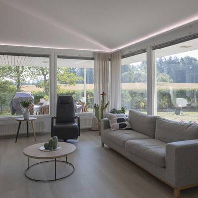 Salon moderne avec plafonniers LED, lampadaire, lumière naturelle provenant de grandes fenêtres, sièges confortables.