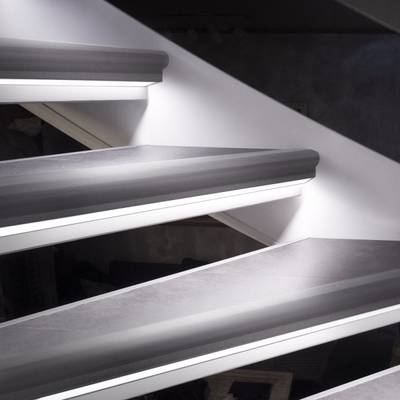 Vue détaillée d'un escalier flottant avec un élégant luminaire LED, un éclairage d'accentuation et un mur blanc.