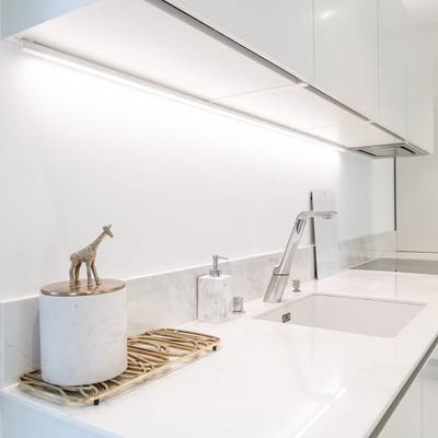 Cuisine moderne avec plan de travail blanc, robinetterie argentée, figure de girafe dans le réservoir ; éclairage LED brillant sous les armoires pour plus d'espace.
