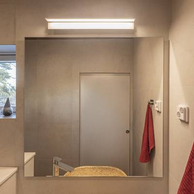 Salle de bains moderne avec éclairage LED à faible consommation d'énergie, grand miroir, comptoir beige, robinet élégant et crochet porte-serviettes rouge pour un intérieur élégant.