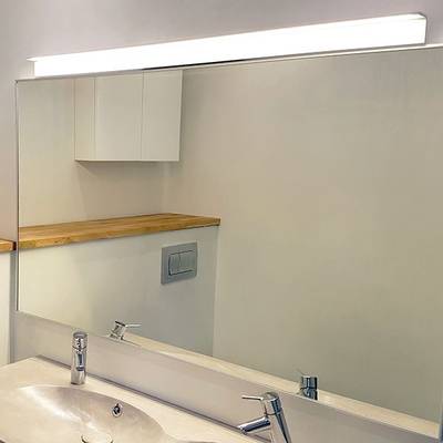 Salle de bains avec miroir éclairé par LED, lavabo et robinets modernes, étagère en bois et armoires blanches. La solution d'éclairage idéale de LED lighting shop.