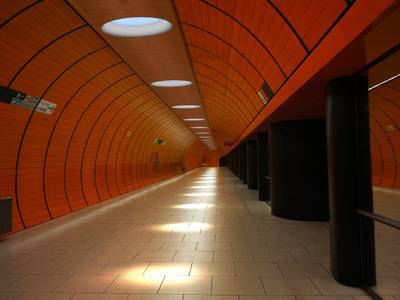 Des plafonniers LED lumineux éclairent un tunnel de métro moderne aux murs orange et au sol carrelé.