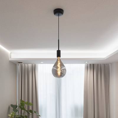 Une lampe suspendue avec ampoule Edison et lampe noire éclaire la pièce avec des rideaux légers et crée une atmosphère chaleureuse.