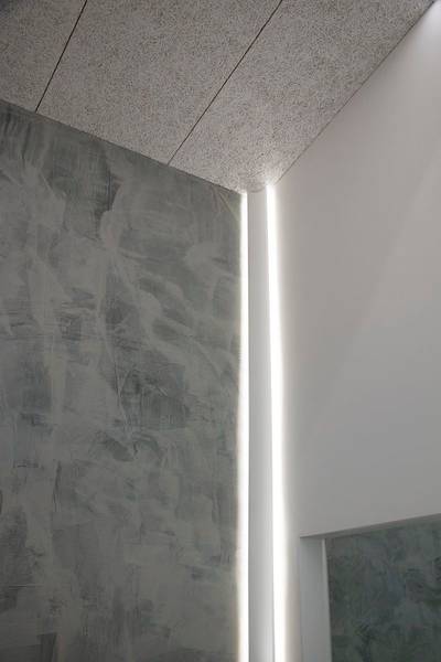 Un mur gris texturé rencontre un mur blanc lisse avec une bande lumineuse LED verticale.