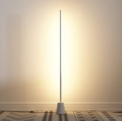 Lampadaire LED minimaliste, au design élancé, qui éclaire le sol et les murs texturés d'une lumière d'ambiance chaleureuse.