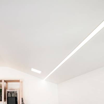 Une pièce moderne avec un plafond incliné, un éclairage linéaire LED encastré élégant et des étagères d'angle avec une variété de produits décoratifs.