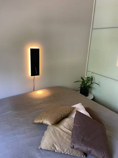 Une chambre à coucher confortable avec un lit bien fait, des coussins, une applique LED rétroéclairée et une plante sur la table de nuit pour une touche de modernité.