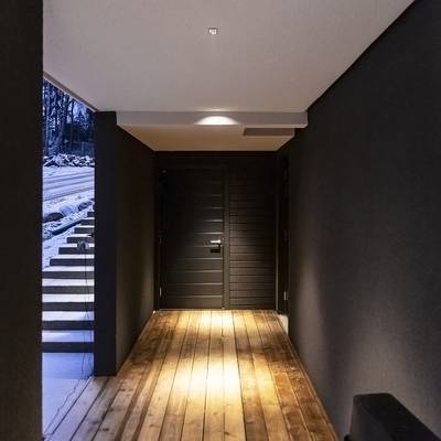 Texte alternatif : hall d'entrée moderne avec murs sombres, sol et escalier en bois éclairés par des LED ; porte noire menant à l'extérieur enneigé. Une atmosphère parfaite pour des intérieurs élégants.