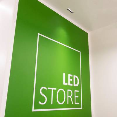 Texte alternatif : "Mur vert avec "LED STORE" contour carré blanc, lettres grasses, lumières au plafond