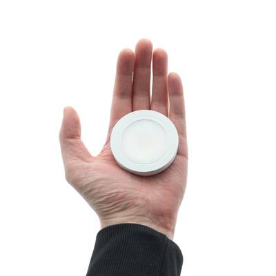 Main tenant un luminaire LED rond sur fond blanc, adapté à l'éclairage intérieur.