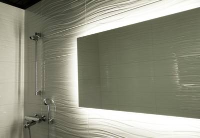 Cette salle de bains moderne présente des carreaux blancs texturés, un grand miroir rétroéclairé, une pomme de douche et un robinet argentés élégants avec un éclairage LED stylisé.