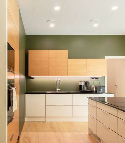 Cuisine moderne avec murs verts, armoires et comptoirs en bois clair, four encastré et îlot assorti, éclairé par des LED élégantes.
