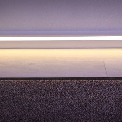 Une bande lumineuse LED moderne éclaire la transition entre la moquette et le plancher en bois, mettant en valeur les détails de la plinthe blanche.
