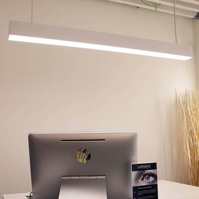 Une lampe de bureau LED élégante qui éclaire un bureau moderne avec un ordinateur sur un bureau blanc ; des branches décoratives dans un grand vase en arrière-plan.