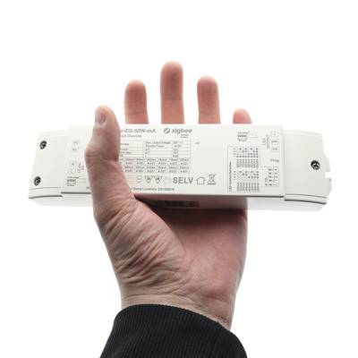 Dans la main, un dispositif rectangulaire blanc affichant des informations techniques et des symboles ainsi que le mot "Zigbee" associé à la technologie d'éclairage LED.