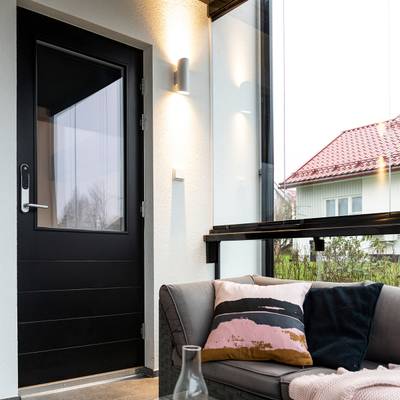Salle de bronzage moderne avec éclairage LED économe en énergie, porte noire, canapé gris avec coussins colorés, murs en verre mettant en valeur la maison avec un toit rouge vibrant.