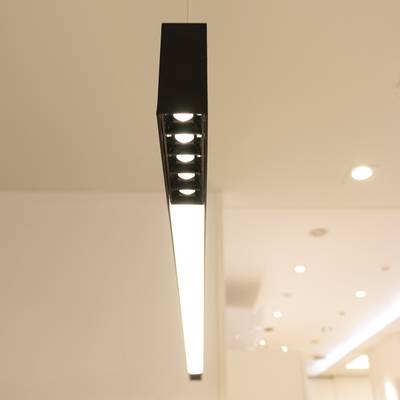 Une lampe suspendue noire moderne avec une lumière blanche brillante dans une pièce minimaliste, mettant en valeur le style contemporain et l'éclairage économe en énergie.