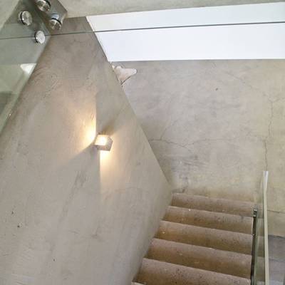 Un escalier moderne avec des marches en béton, une balustrade en verre et une lampe LED murale qui brille chaleureusement ; le design minimaliste ajoute à l'ambiance.