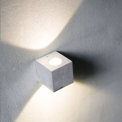 Une applique cubique minimaliste avec un mur à motifs diffuse une lumière douce et diffuse vers le haut et vers le bas, mettant en valeur un intérieur moderne.