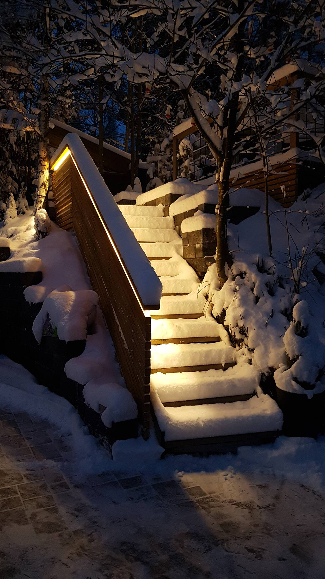 Éclairage d\'un escalier extérieur réalisé avec une bande de LED sur la balustrade. La lumière est une lumière indirecte atmosphérique, la bande LED utilisée est une bande chaude 3000K 7,2W/m. Ledstore.fi