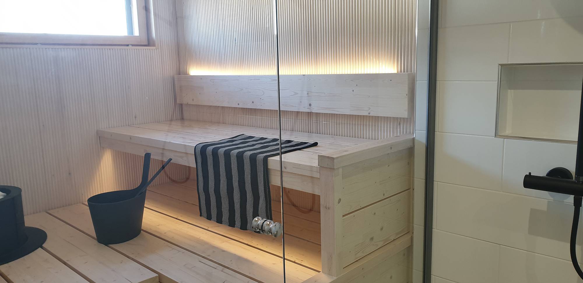 Une bande LED à l\'arrière du dossier du sauna diffuse une lumière d\'ambiance vers le haut et vers le bas, sous le plafond. Ledstore.fi