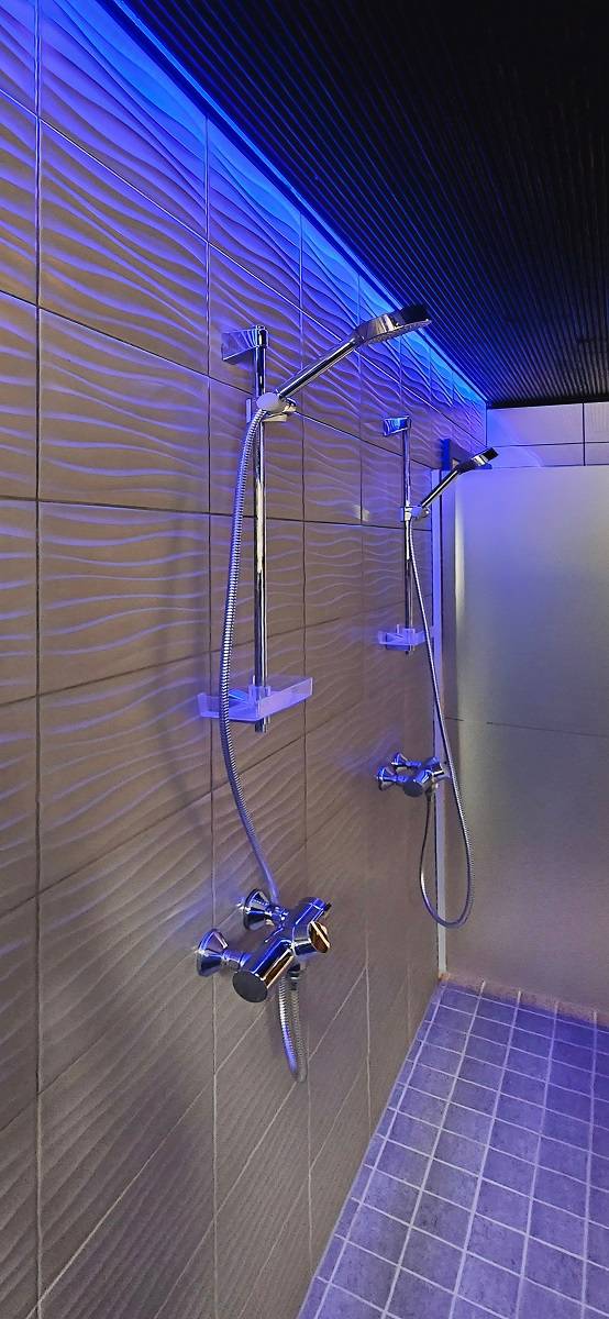 Les toilettes des hommes sont éclairées par des bandes lumineuses RVB depuis le plafond au-dessus des douches, photo de The Goonies