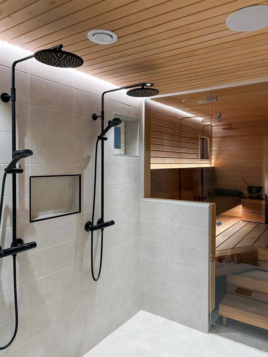 Derrière les douches, une bande lumineuse LED placée dans une rainure du plafond éclaire indirectement le mur jusqu'au sol. La lumière est à la fois efficace et agréable à l'œil. ledStore.fi