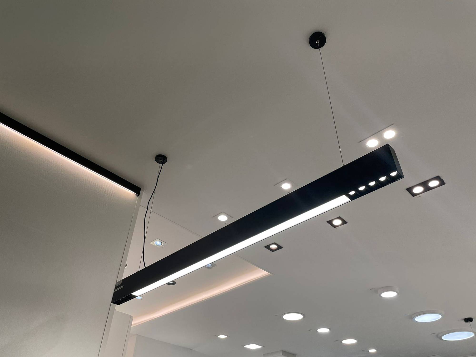 Luminaire Ledstorella Line au-dessus du comptoir de vente. Bande LED sur un profilé d\'aluminium de remplacement dans le plafond pour fournir une lumière indirecte, des spots et des panneaux lumineux au plafond. Ledstore.fi