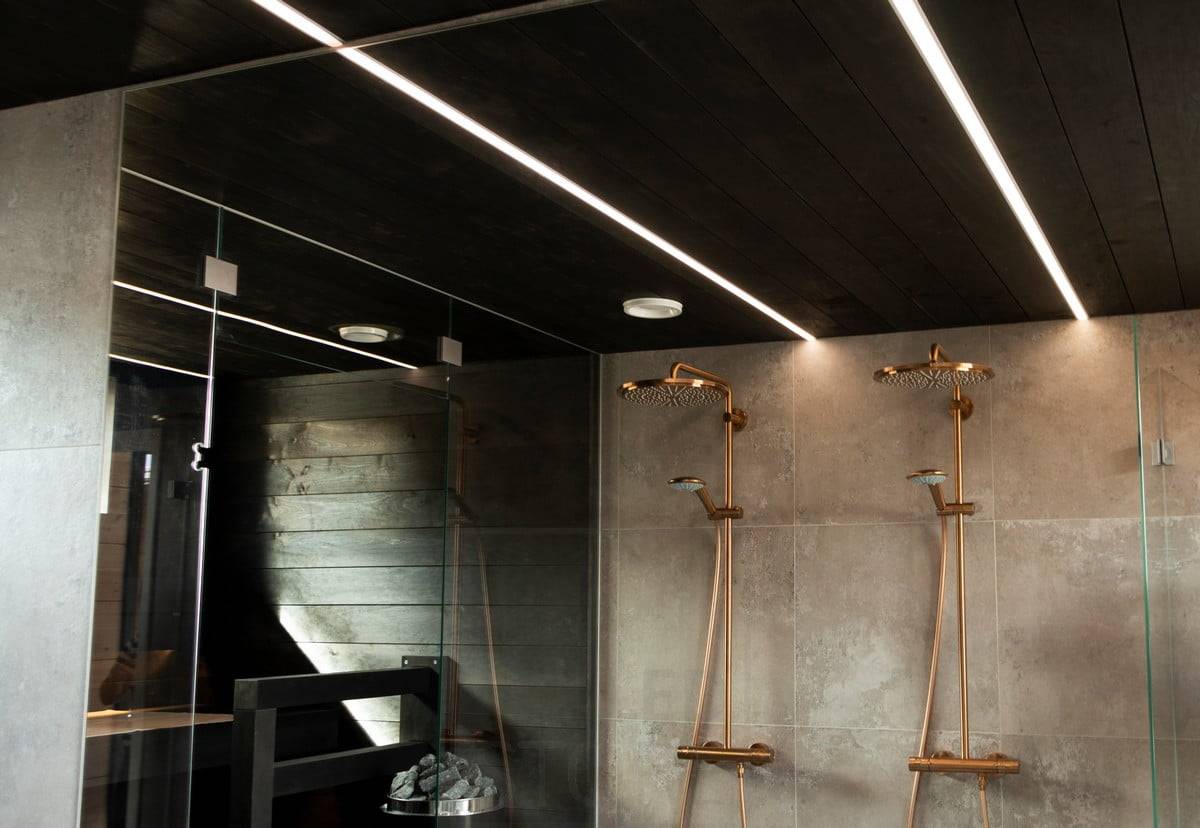 Salon du logement 2020 : des bandes de LED éclairent la salle de bain dans des profils encastrés étroits dans le plafond noir de la salle de bain. Les lignes lumineuses éclairent l'espace avec une lumière agréable et de haute qualité. Ledstore.fi