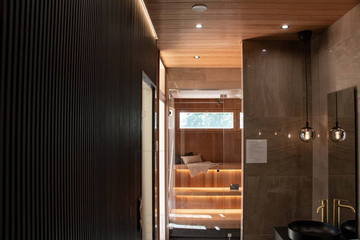 Salon du logement 2022 : éclairage d'ambiance dans les toilettes et le sauna. La lumière indirecte met en valeur la corniche murale et les bandes LED sous le plafond du sauna. La lampe suspendue est un bel élément décoratif. Ledstore.fi