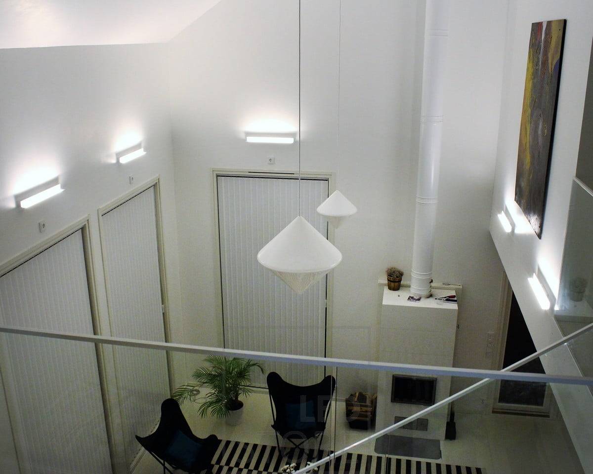 Un éclairage indirect atmosphérique pour le salon avec les appliques Led BLADE. Le luminaire est monté de manière à éclairer du bas vers le haut, ce qui permet à l'éclairage indirect de souligner la hauteur de l'espace et les œuvres d'art sur le mur. Ledstore.fi