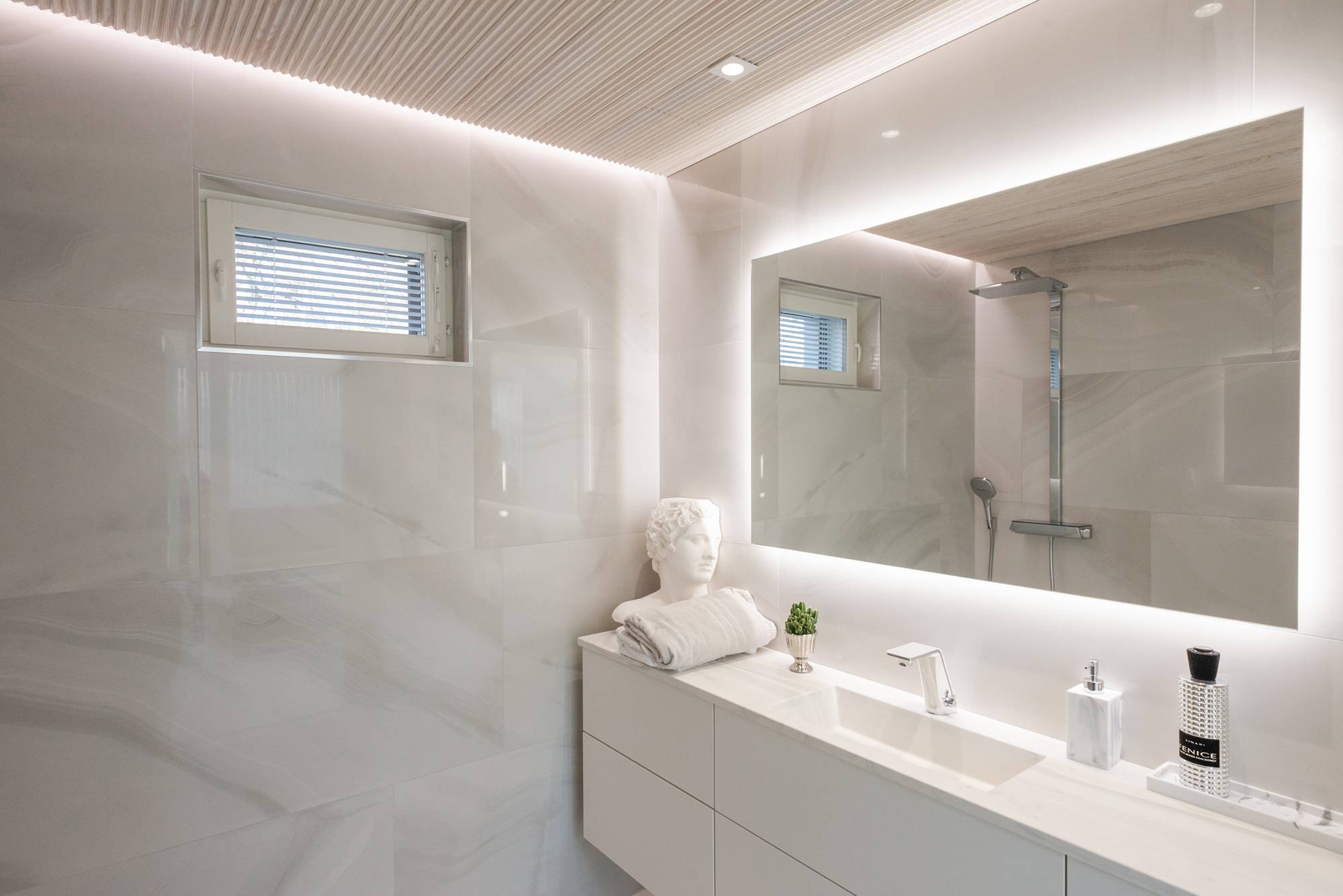 Dans une salle de bains équipée d\'une baignoire spa, un grand miroir lumineux est combiné à des spots et à une bande LED allant du mur au plafond.