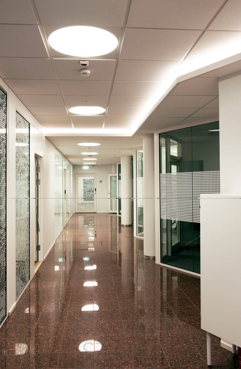 Bande LED montée sur le downlight d'un couloir créant une lumière indirecte atmosphérique à travers le plafond. L'éclairage général est assuré par des luminaires encastrés Plafondi.