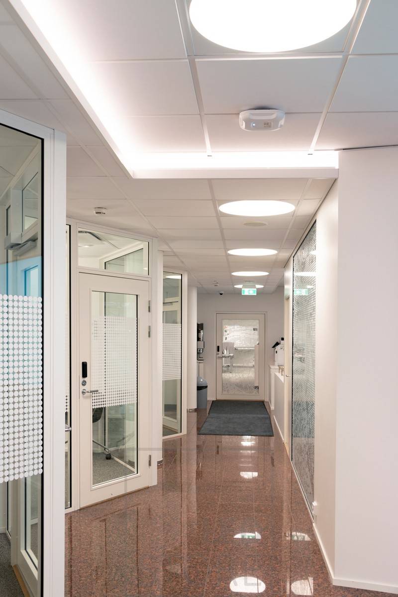 Bande LED montée sur le downlight d'un couloir créant une lumière indirecte atmosphérique. L'éclairage général est assuré par des luminaires encastrés Plafondi.