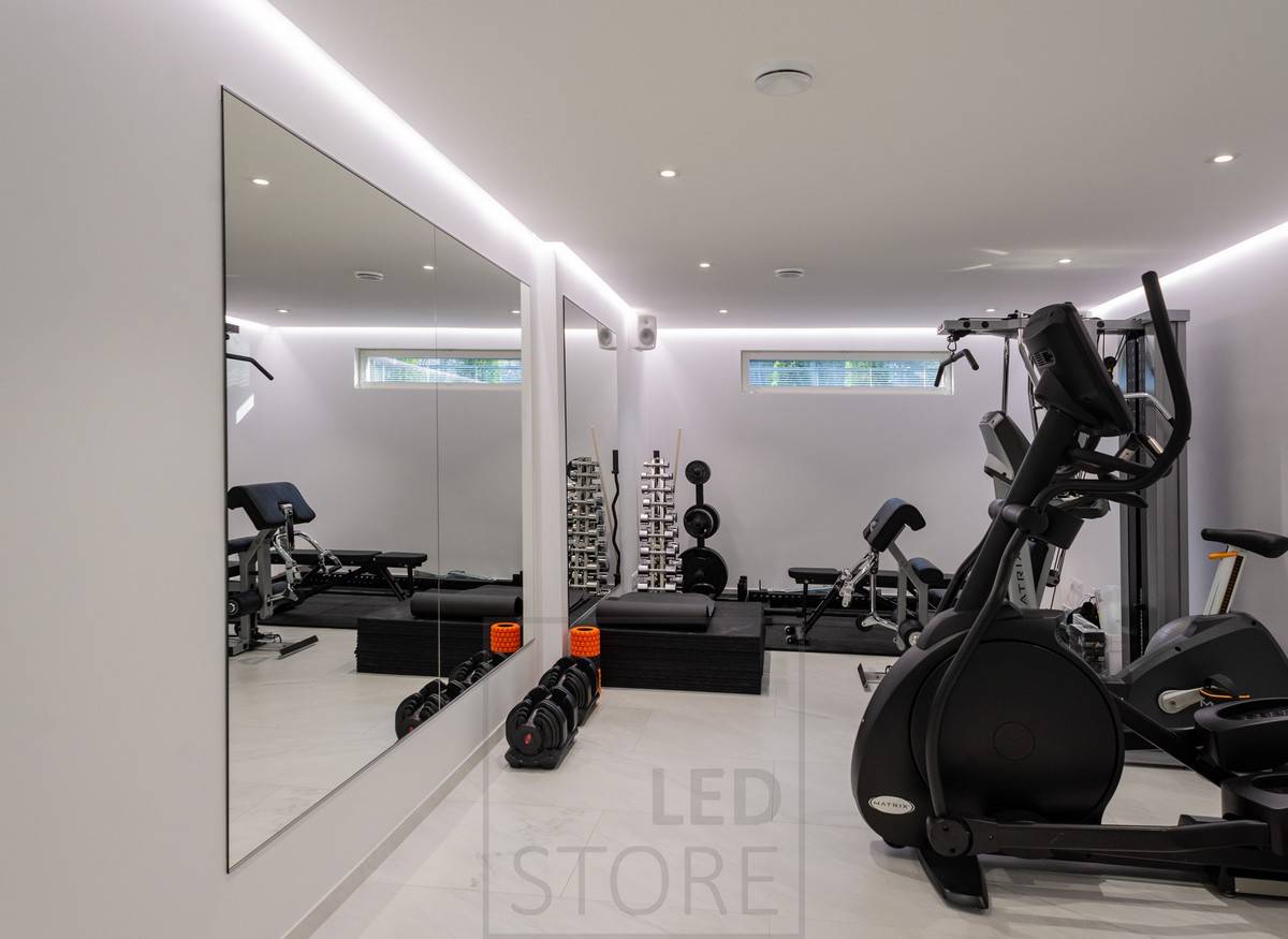 Salle de sport éclairée par des spots et une lumière indirecte d'ambiance. L'éclairage indirect est obtenu grâce à une bande lumineuse LED installée entre le plafond et le mur.