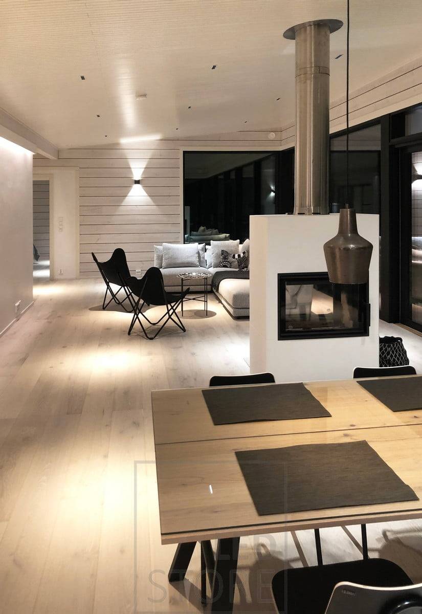 L'applique FUNK noire éclaire le salon d'une lumière d'ambiance à travers le mur. Pour l'éclairage général de l'espace, les spots LINJA 2 éclairent la lumière à angle étroit. Ledstore.fi