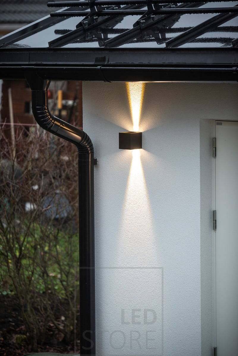 Appliques FUNK noires bidirectionnelles éclairant la façade du garage. La lumière ascendante s'arrête au niveau de l'avant-toit. Ledstore.fi