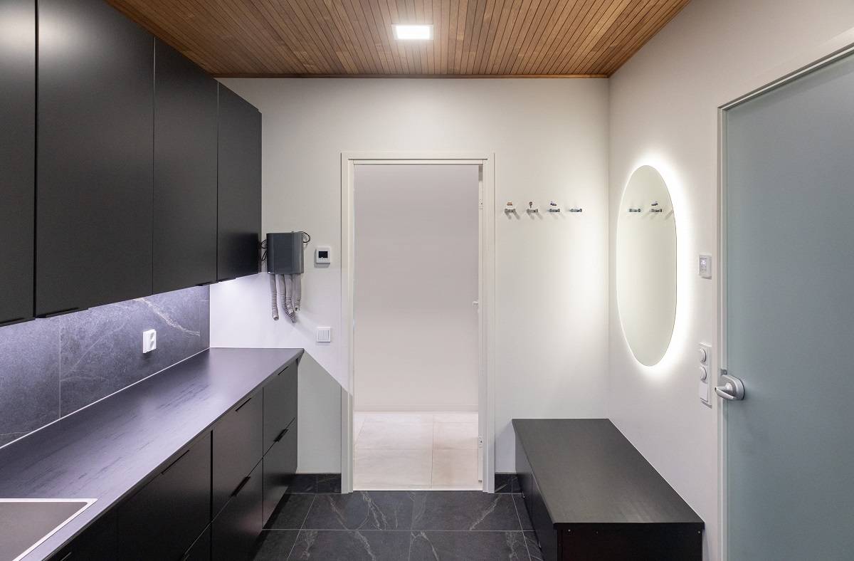 Au plafond d'une salle de soins à domicile, une petite lampe rectangulaire, un miroir ovale et une bande LED éclairent le plan de travail.