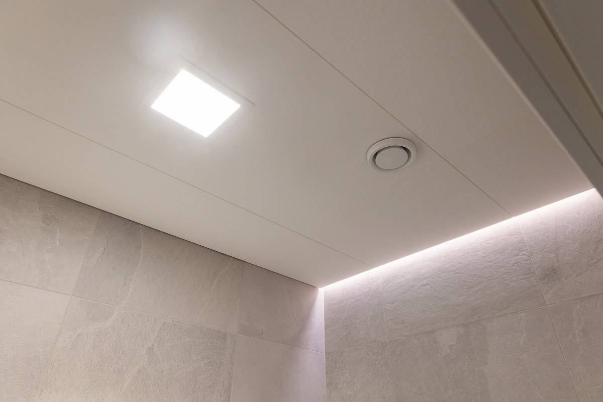 Bande LED dans le renfoncement entre le plafond et le mur et petit panneau LED carré encastré dans le plafond.