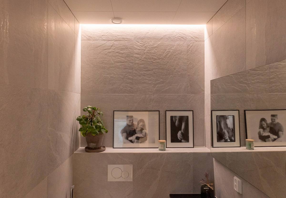 Bande LED à température de couleur chaude encastrée entre le mur et le plafond d'une salle d'eau.