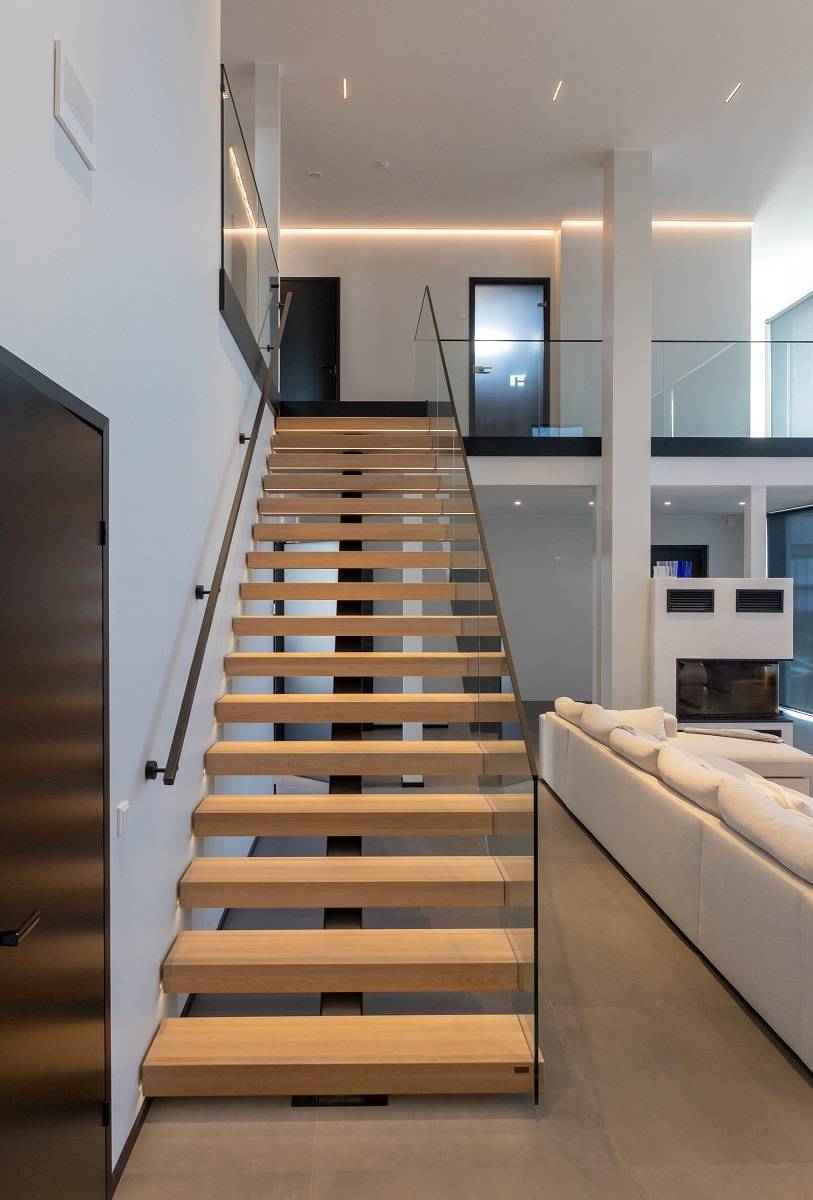 Escalier en bois clair menant à l'étage éclairé par un bandeau de leds et un bandeau de leds faisant le tour du mur à l'étage supérieur