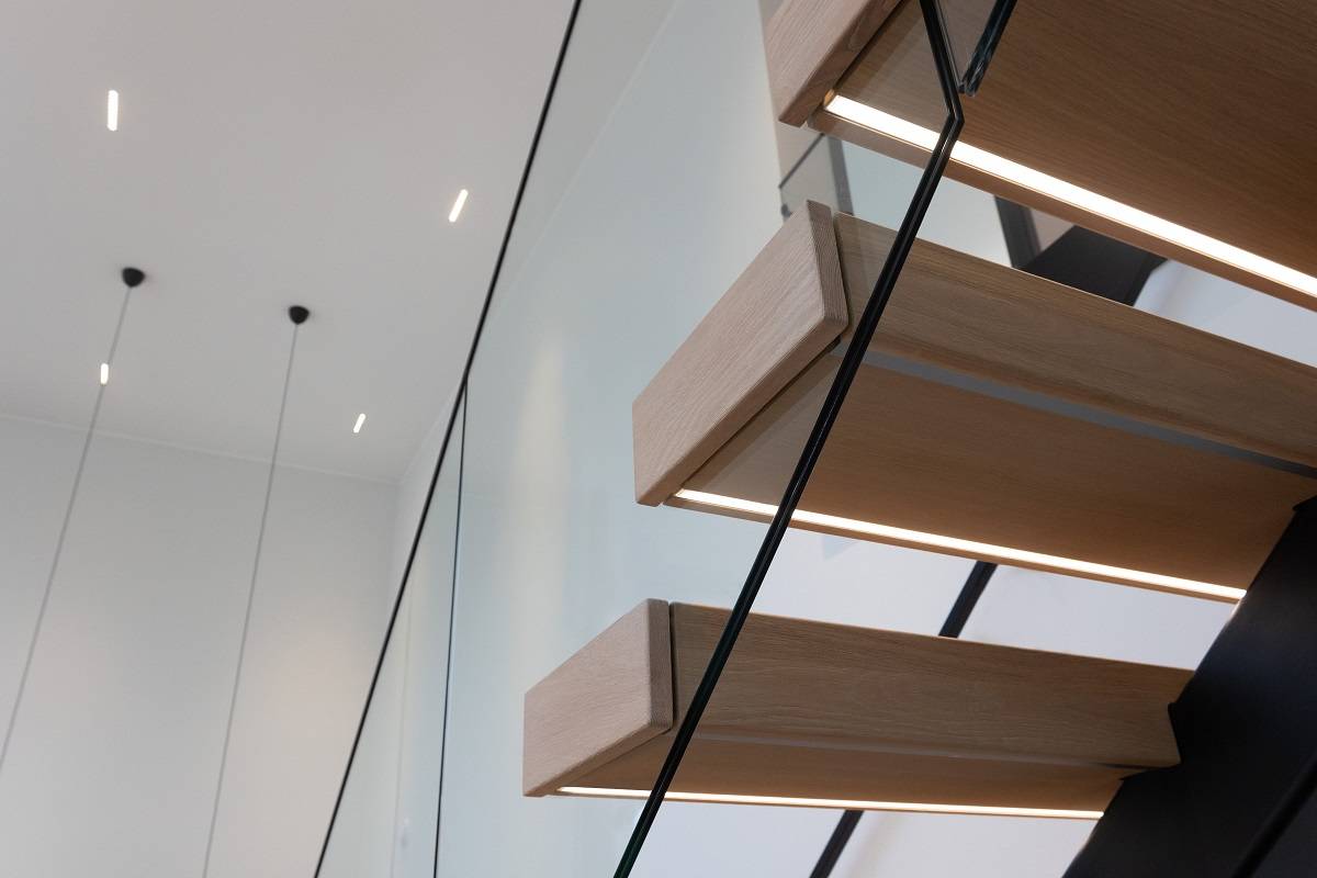 Sous la marche d'escalier, bande LED encastrée de profil. Spots led LINJA10 en arrière-plan au plafond.
