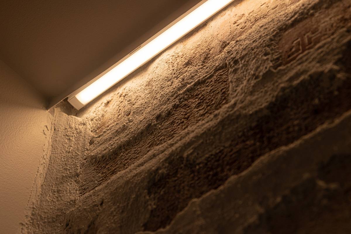 Gros plan sur l'installation d'une bande LED sur un mur d'accent. La bande LED est installée dans un profilé en aluminium en applique, entre la moulure et le mur.