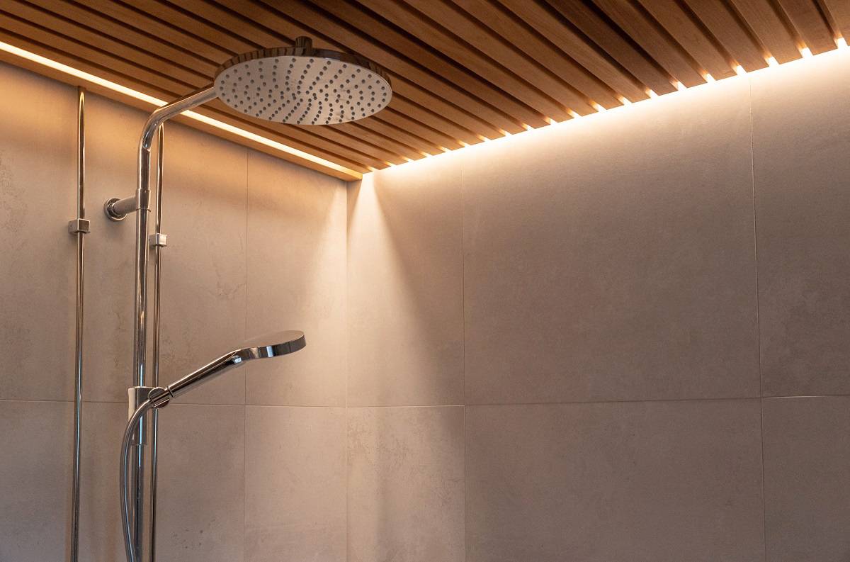 Une bande LED est encastrée dans le plafond à lattes de la salle de douche.