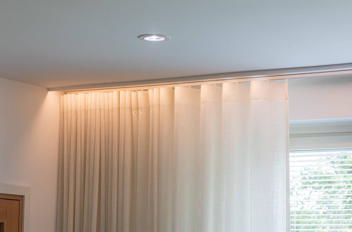 Éclairage vers le bas au plafond du salon. Devant le rideau, une bande LED est installée derrière la moulure, ce qui permet de dissimuler la source lumineuse.