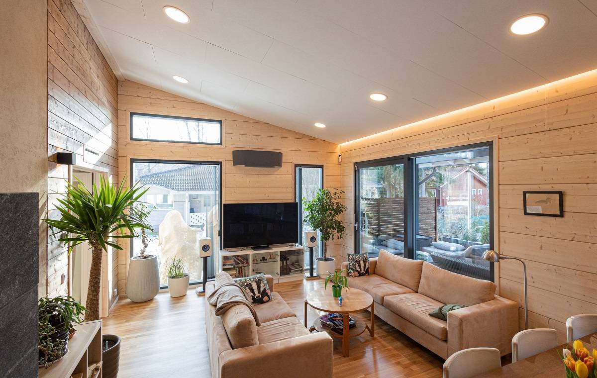 Salon avec des surfaces en bois clair et un plafond clair. Panneaux encastrés circulaires au plafond et bandeau de LED à la jonction mur/plafond.