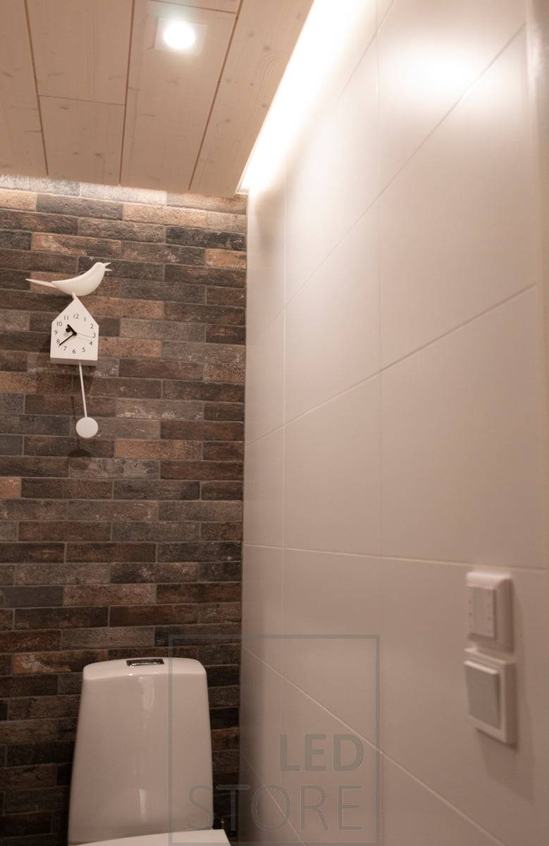 Eclairage avec downlight LED - LIGHT GREEN R023 et éclairage indirect avec profilé de surface blanc dans la rainure du plafond avec une bande CCT de 7,2 W/m. Un contrôleur sans fil monté au-dessus de l'interrupteur est également visible sur le mur.